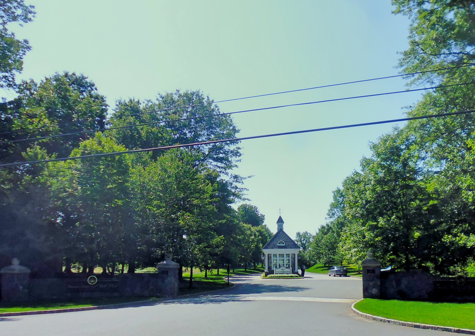 The gatehouse and stone entrance to Trump National Golf Club in Bedminster, New Jersey, photographed from the road on a summer day.