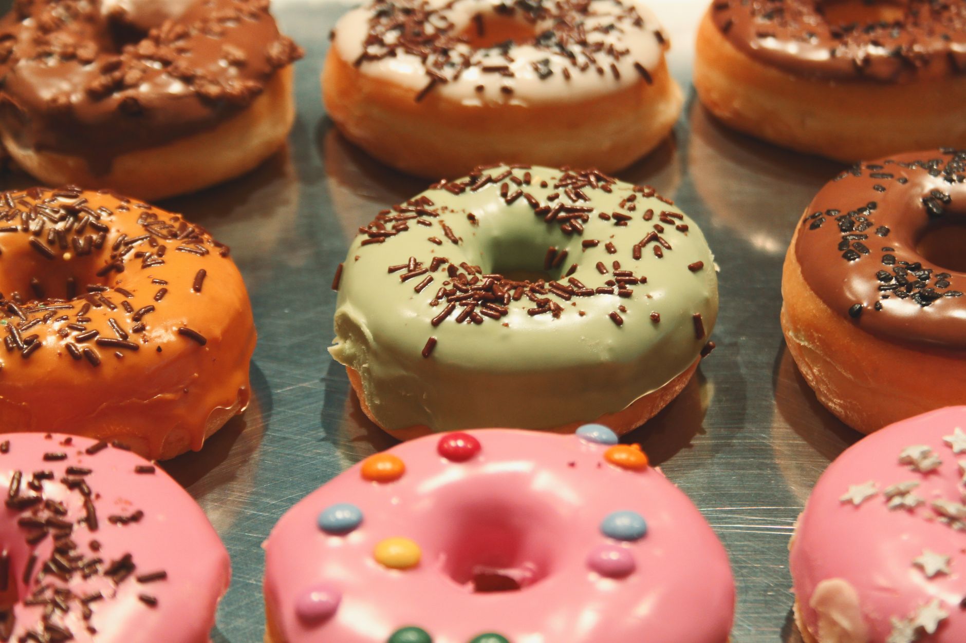 An assortment of glazed and sprinkle-topped donuts on a display tray.