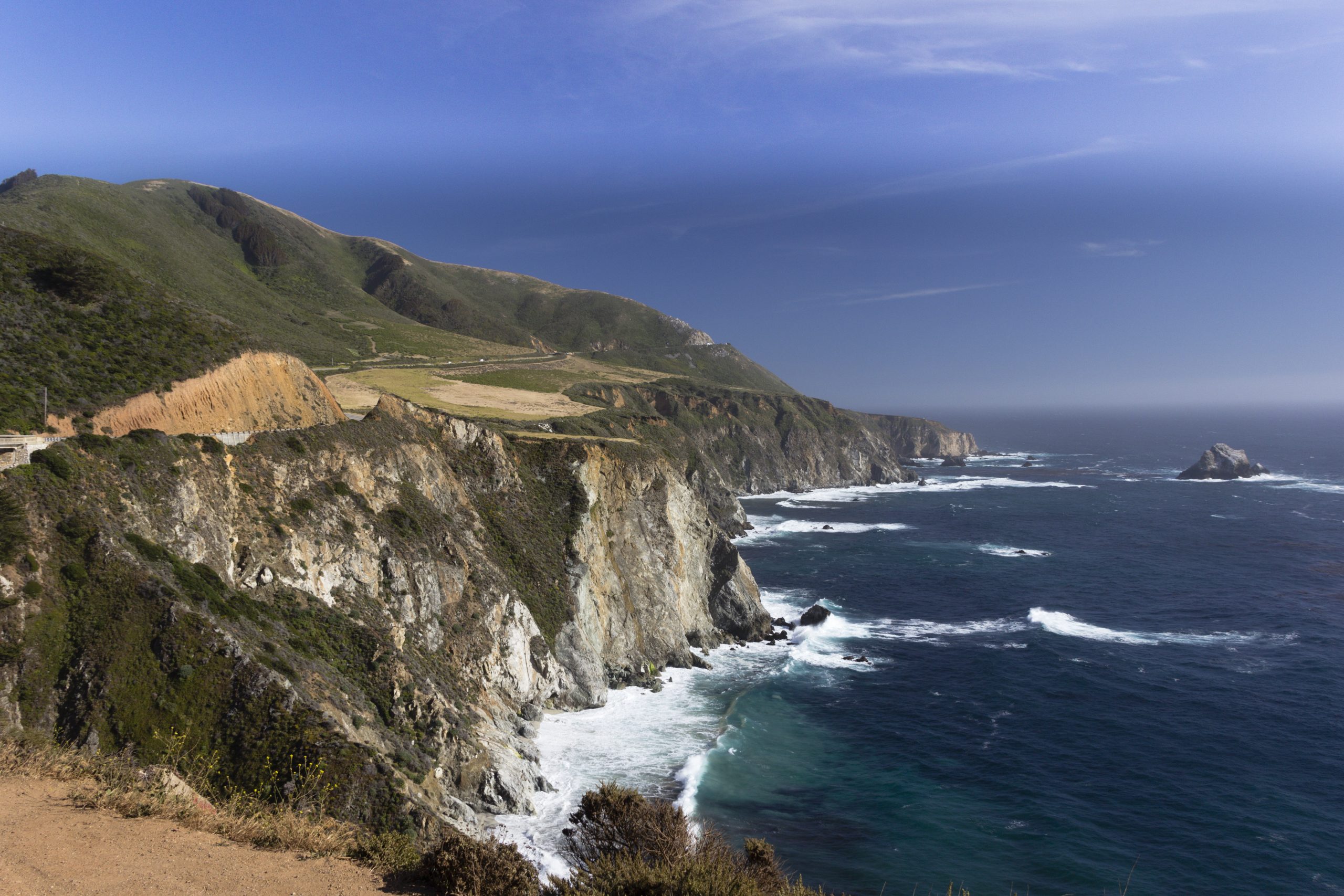 Coastal bluffs along California's Big Sur shoreline, with Highway 1 running along the ridge above the Pacific Ocean.