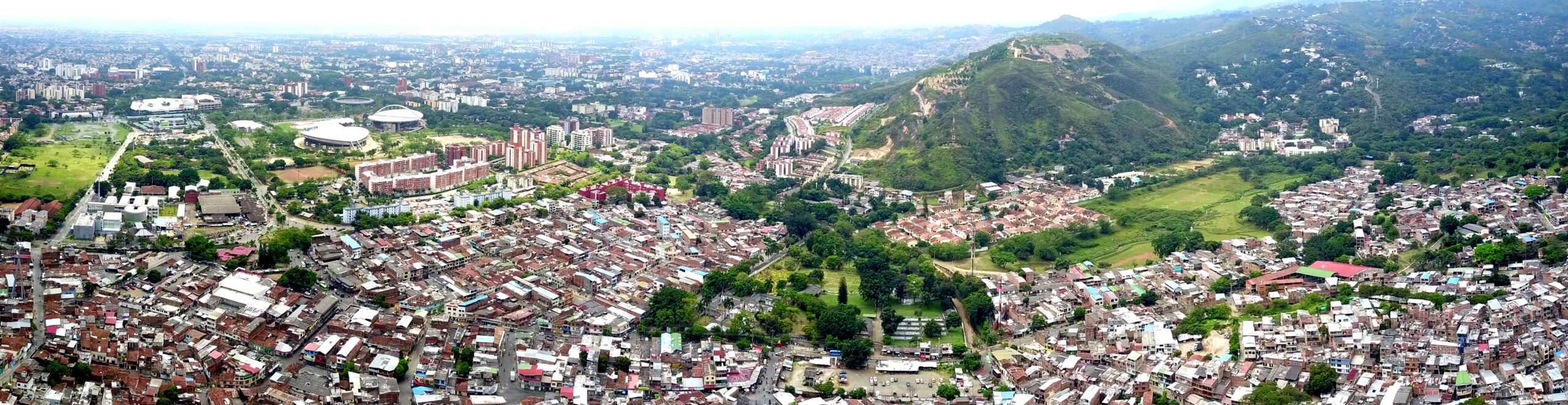 Aerial view of Cali, Colombia, showing dense low-rise neighbourhoods, apartment blocks and the green hills on the city's western edge.