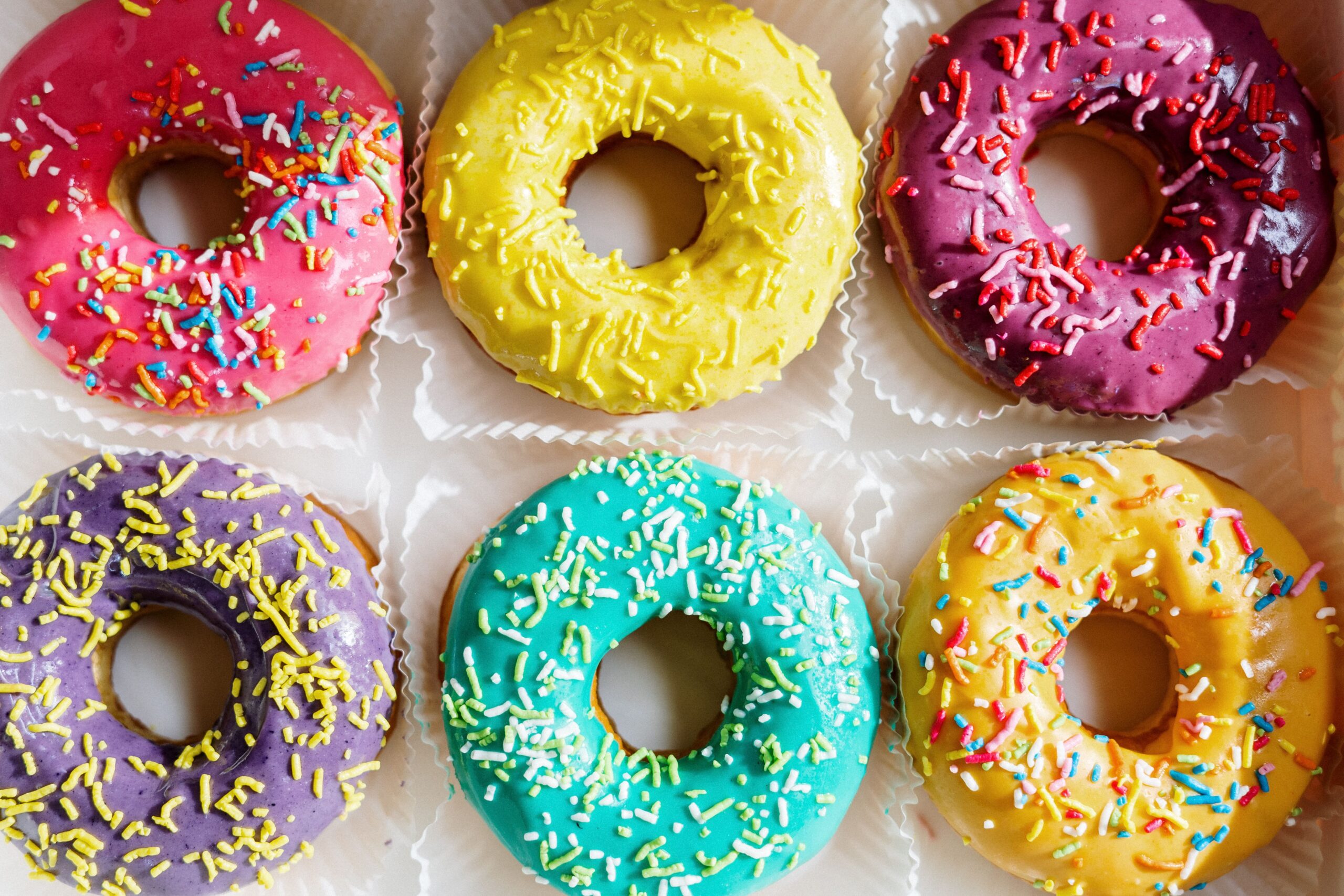 A box of six colorful glazed doughnuts topped with sprinkles