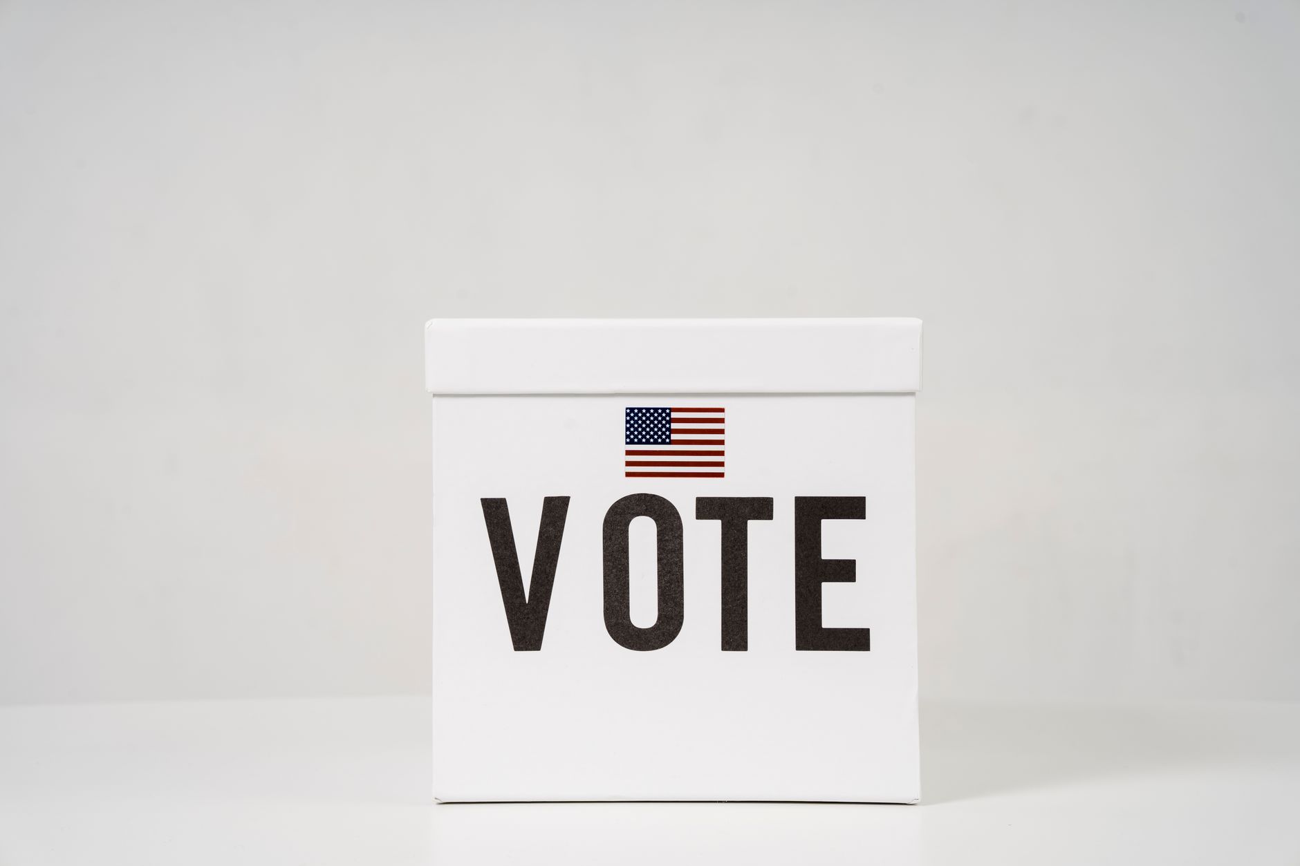 Photo: A minimalist ballot box with 'Vote' and an American flag, symbolizing elections.