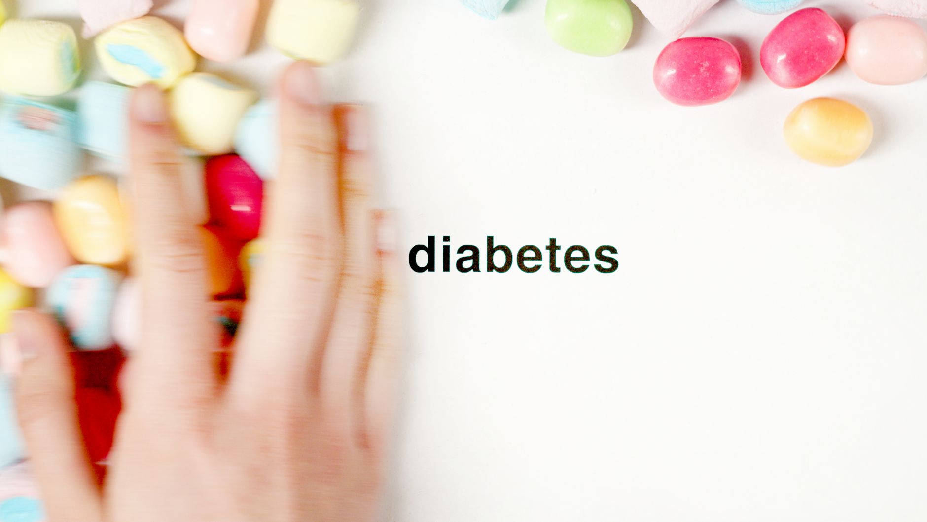 Hand reaching toward colorful candy near the word diabetes, symbolizing blood-sugar management