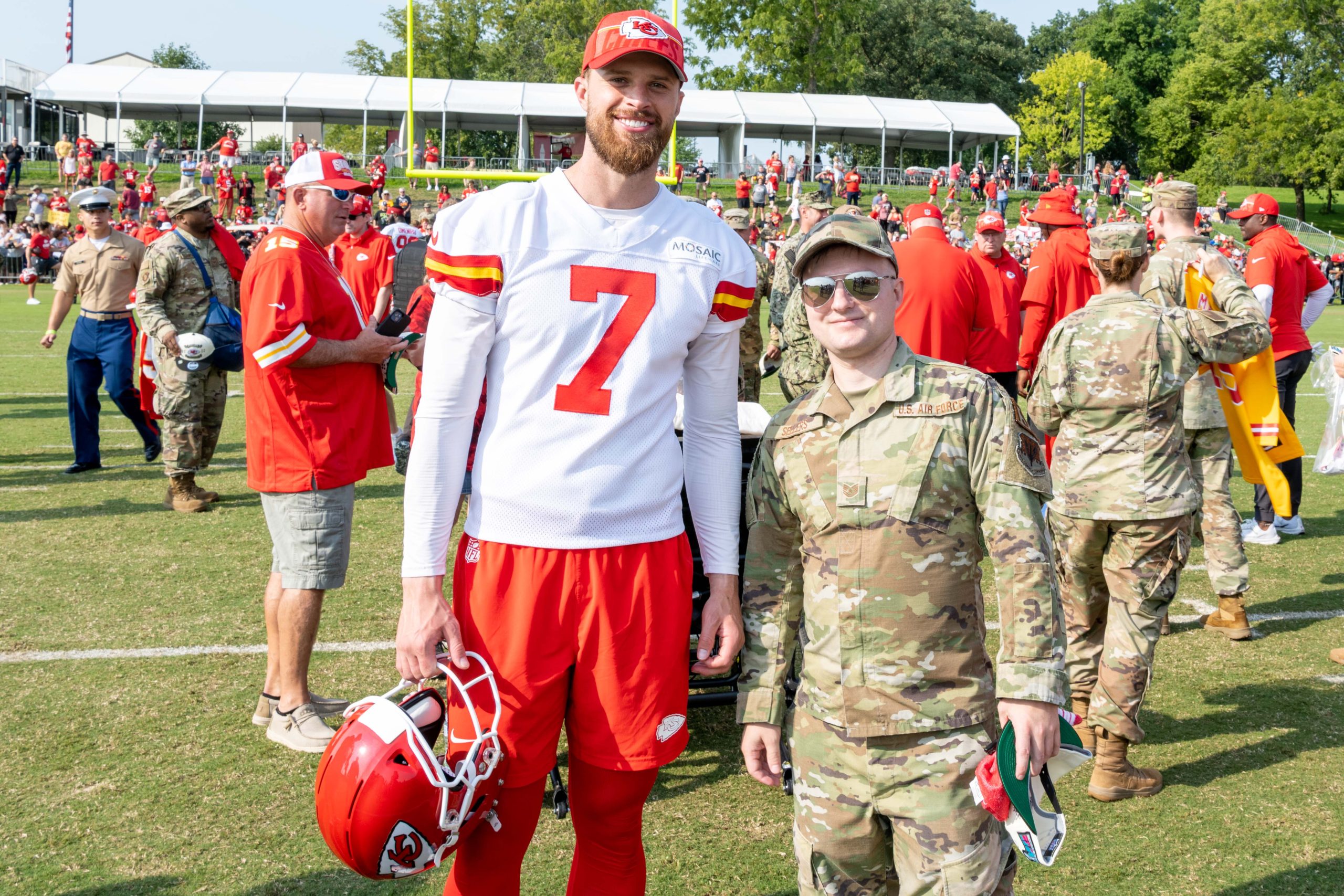 Kansas City Chiefs kicker Harrison Butker, in a Chiefs jersey and cap, poses with a U.S. Air Force service member at training camp
