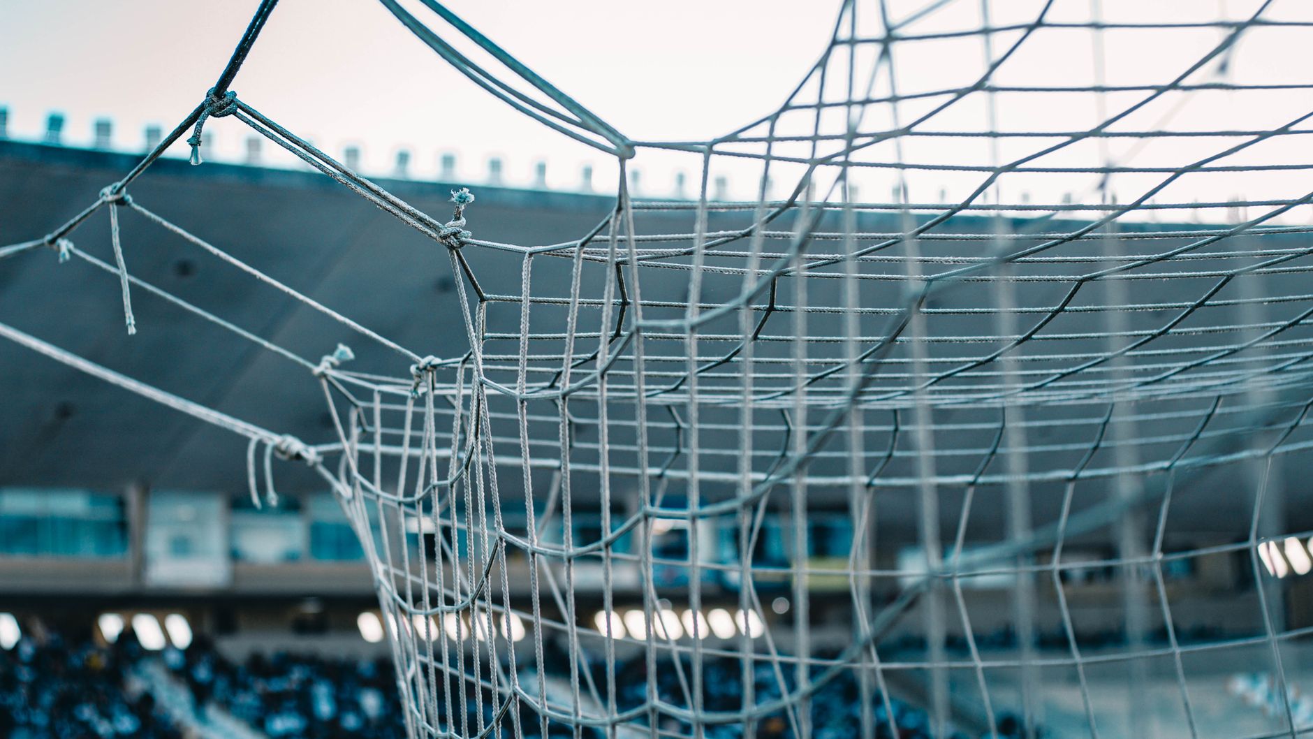 Photo: A detailed view of a soccer net with stadium seating in the background.