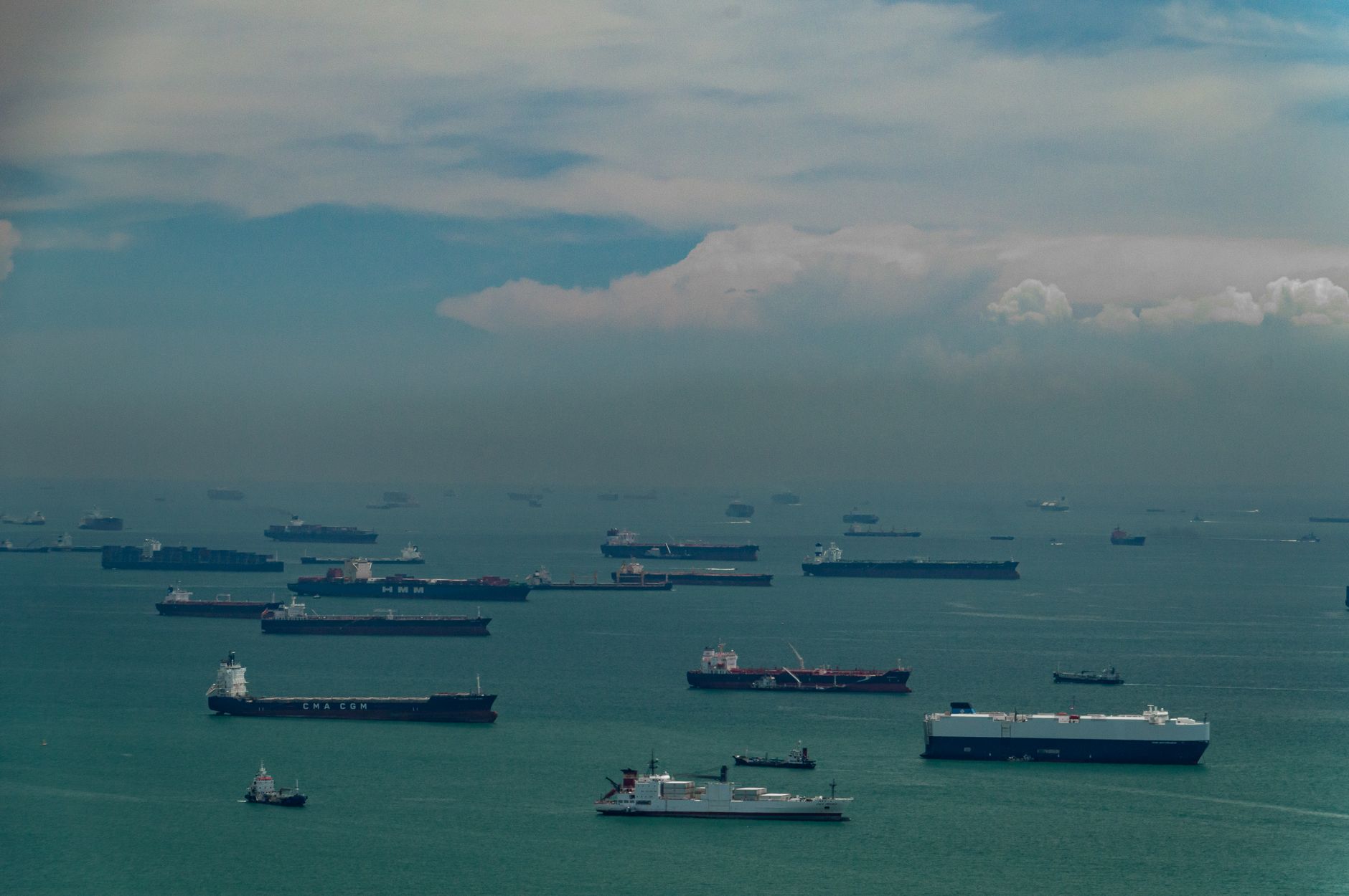 Editorial photo-illustration: cargo ships and oil tankers anchored in a busy shipping lane, illustrating global maritime trade routes.