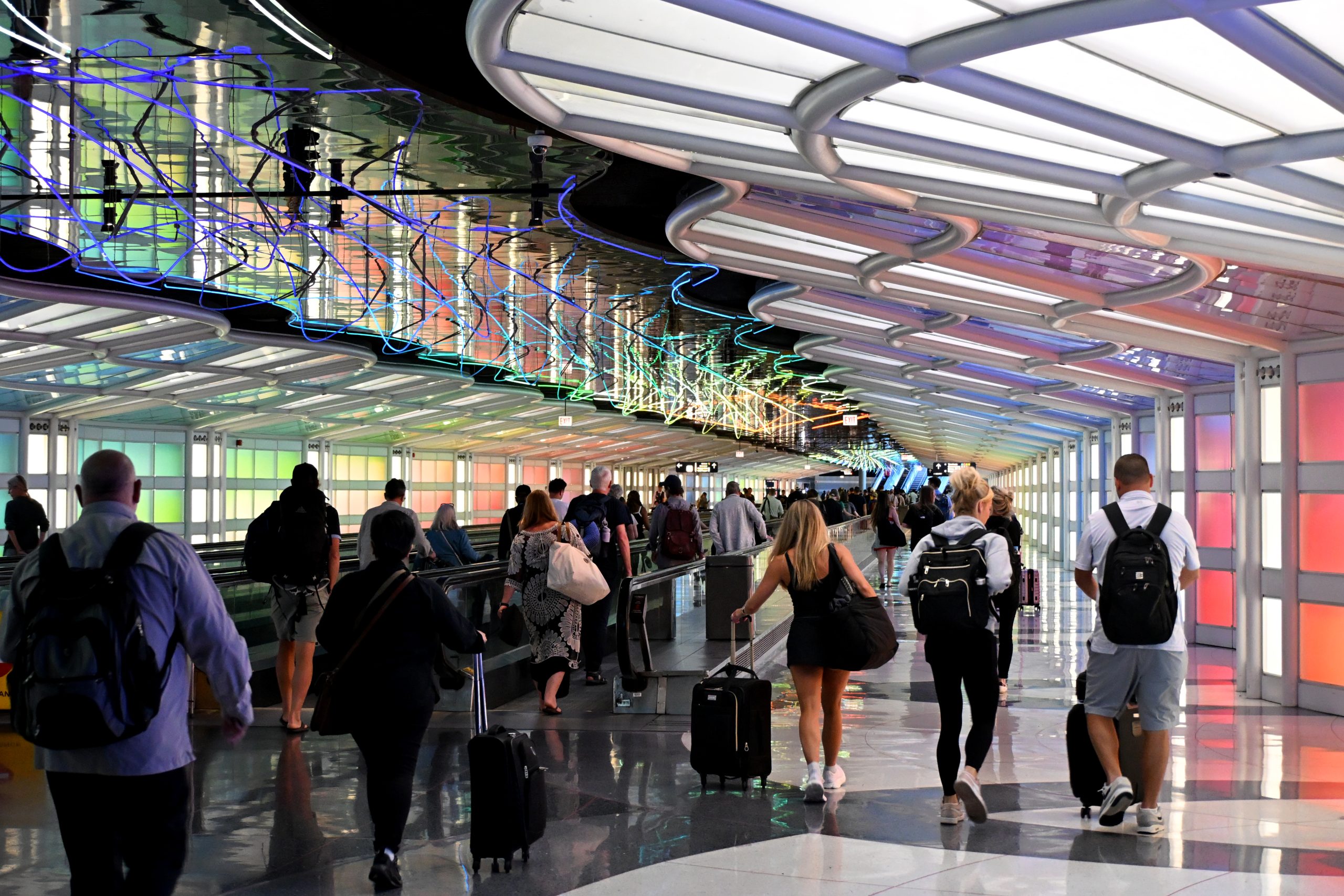 Travellers with wheeled luggage walk and ride the moving walkways through the neon-lit underground pedestrian tunnel connecting concourses at O'Hare International Airport in Chicago.