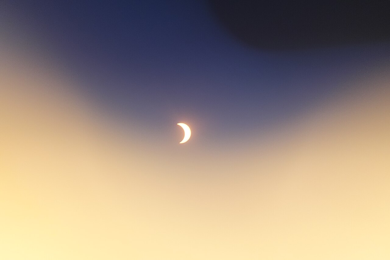 A crescent Sun partly covered by the Moon during the partial phase of the August 12, 2026 solar eclipse, seen against a clear graded twilight sky.