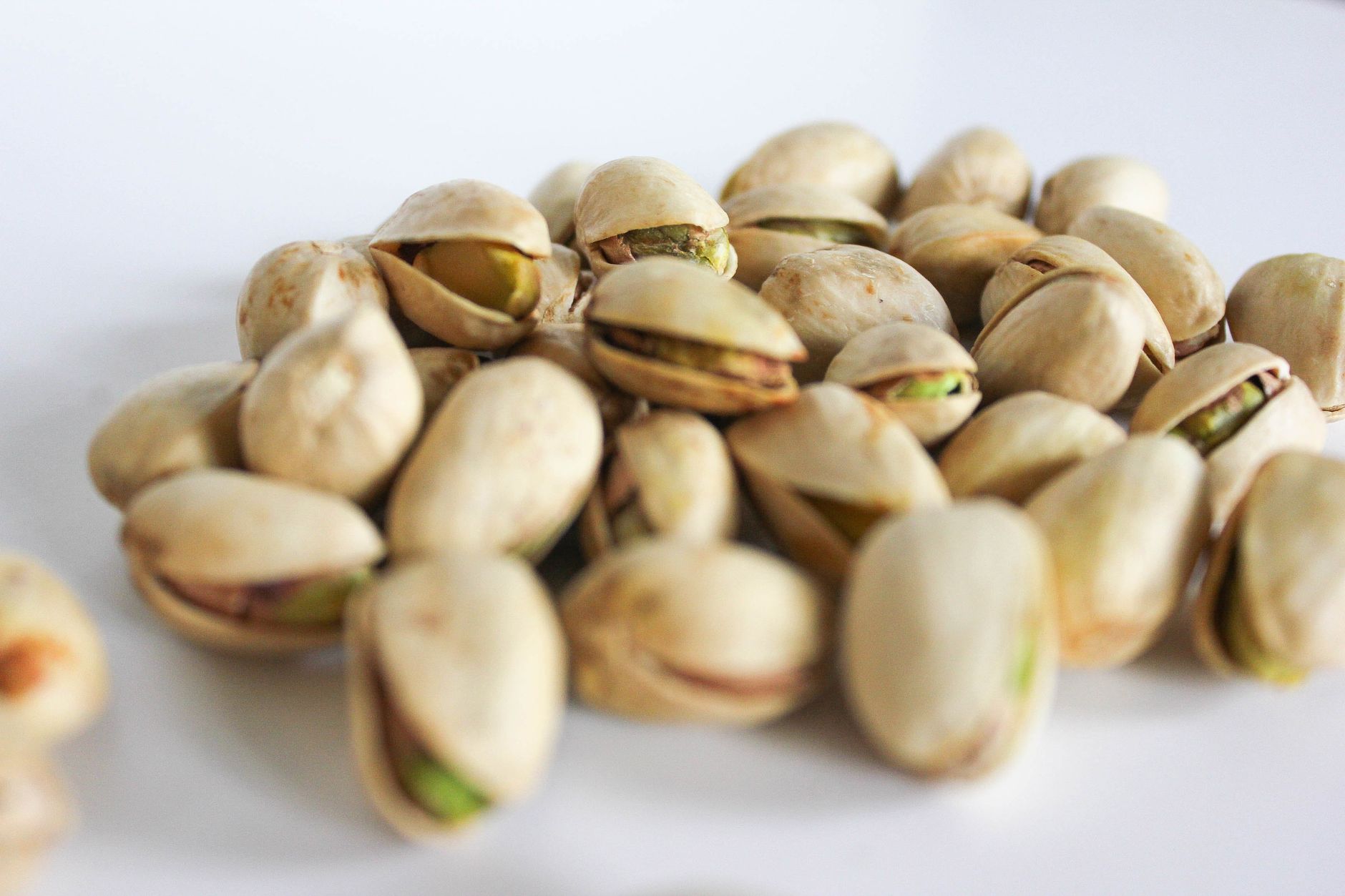 Photo: A close-up of fresh pistachio nuts scattered on a white surface, showcasing their natural shells and vibrant color.