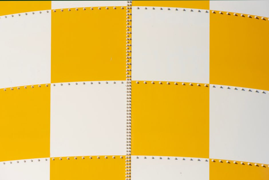 Photo: Close-up of a yellow and white checkered aircraft-style metal panel with rows of rivets.