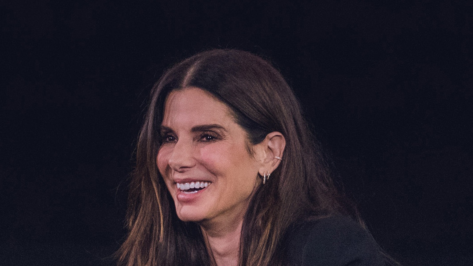 Sandra Bullock smiling during a public conversation event in October 2024, wearing a black outfit, seated with a microphone.