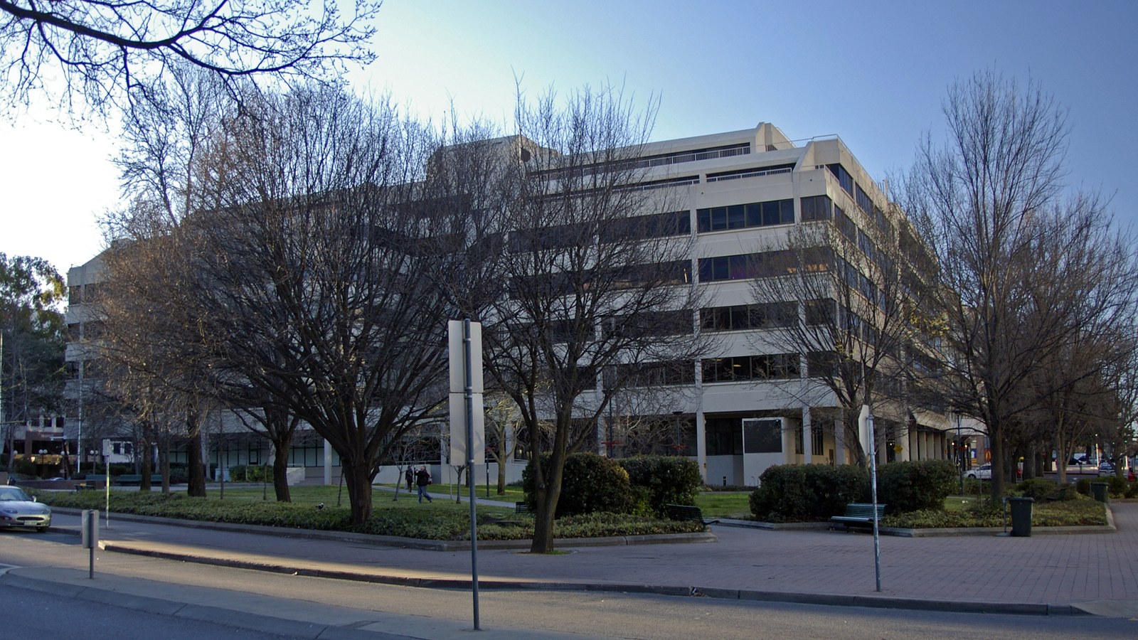The Australian Federal Police headquarters in Canberra, a low modern office block of pale concrete and dark glass behind bare winter trees on a city street.