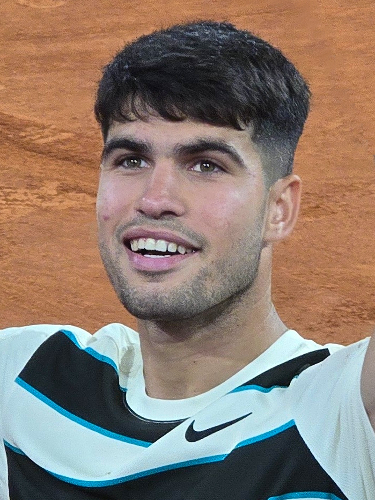 Carlos Alcaraz smiling on court, wearing a Nike shirt, at the 2025 French Open