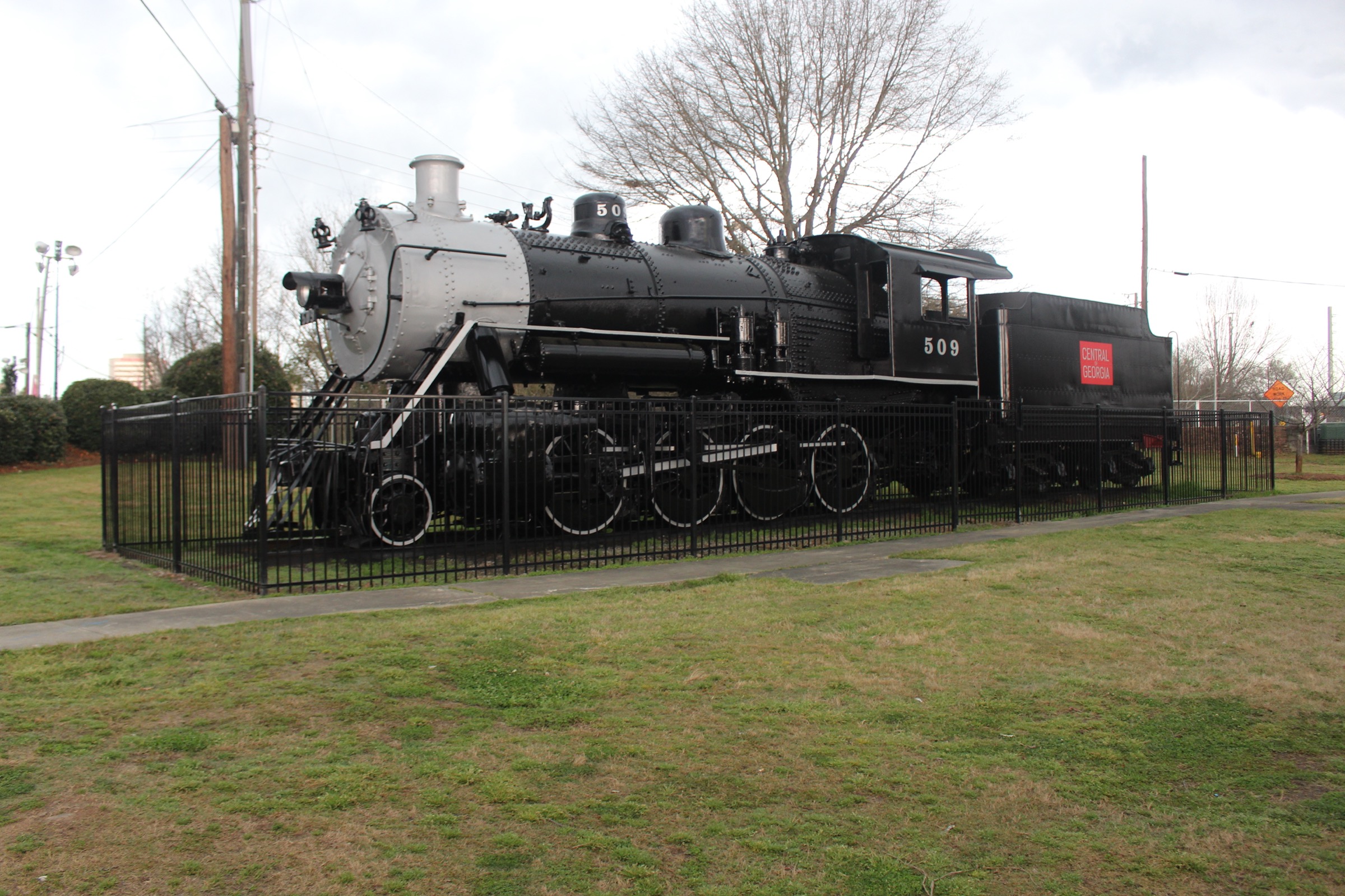A black Central of Georgia steam locomotive, number 509, displayed behind an iron fence on a lawn in Carolyn Crayton Park in Macon, Georgia.