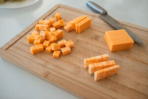Cubes and slices of orange cheddar and marbled colby-jack cheese on a wooden cutting board beside a knife.