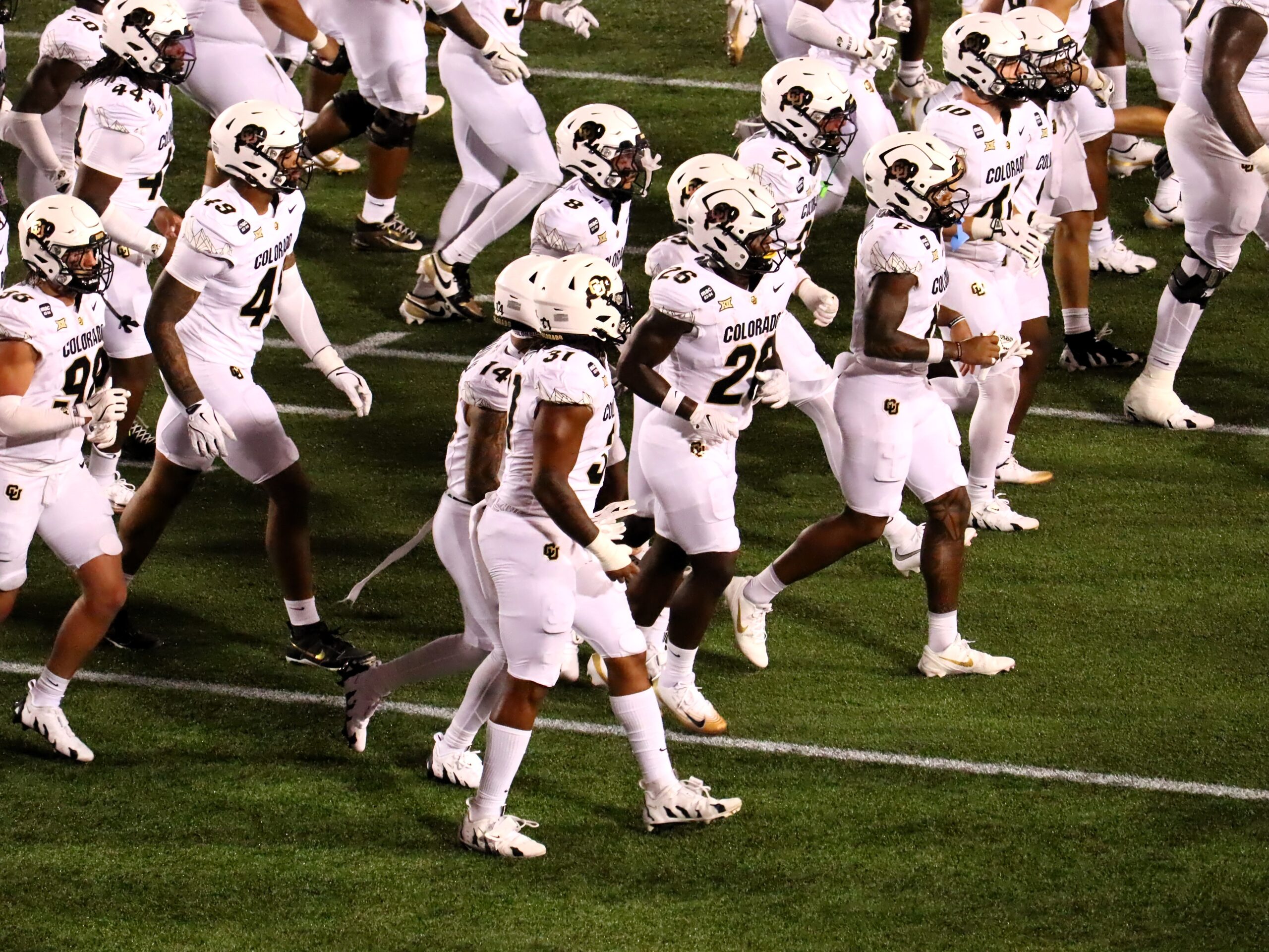 Colorado Buffaloes football players in white Colorado uniforms and helmets running onto the field