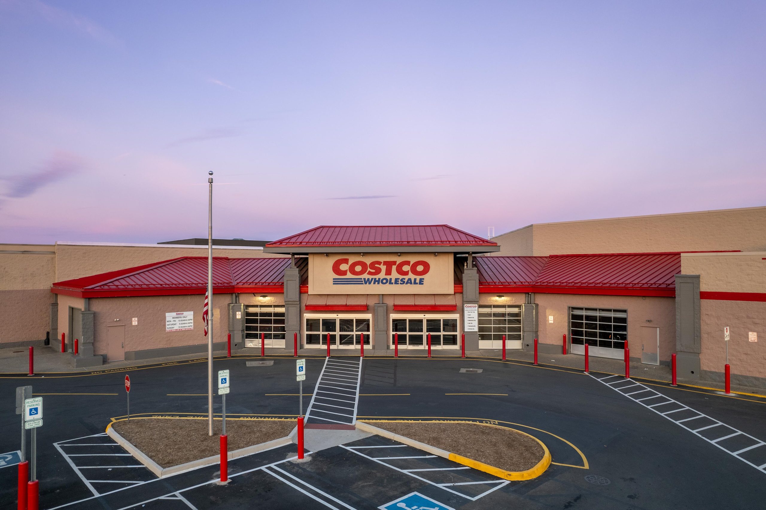 The entrance of a Costco Wholesale warehouse store in Fredericksburg, Virginia, with its red roof and an empty parking lot at dusk.