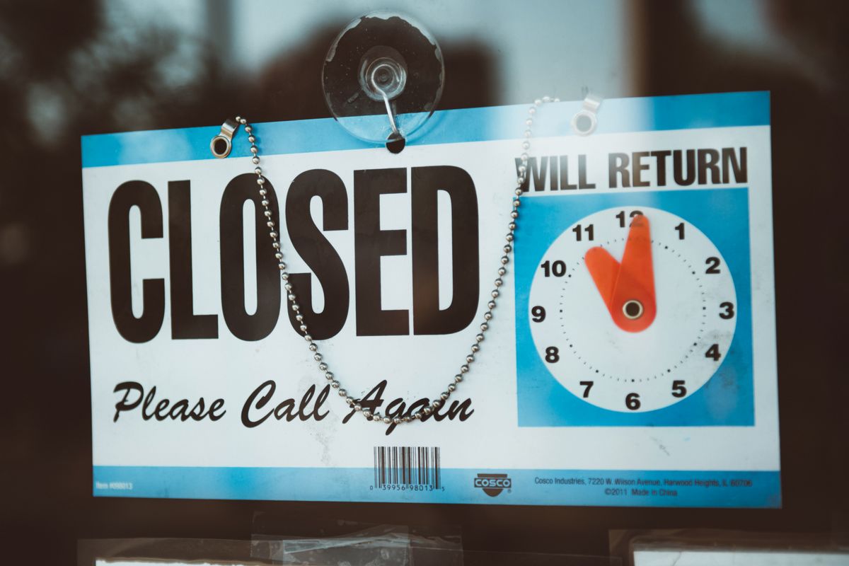 A generic blue and white "Closed, Please Call Again" sign with a Will Return clock hangs in a glass door.