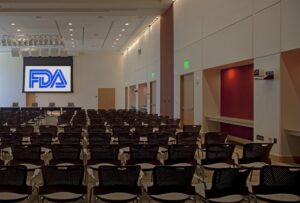 Rows of empty chairs face a projection screen showing the FDA logo in a large conference room.