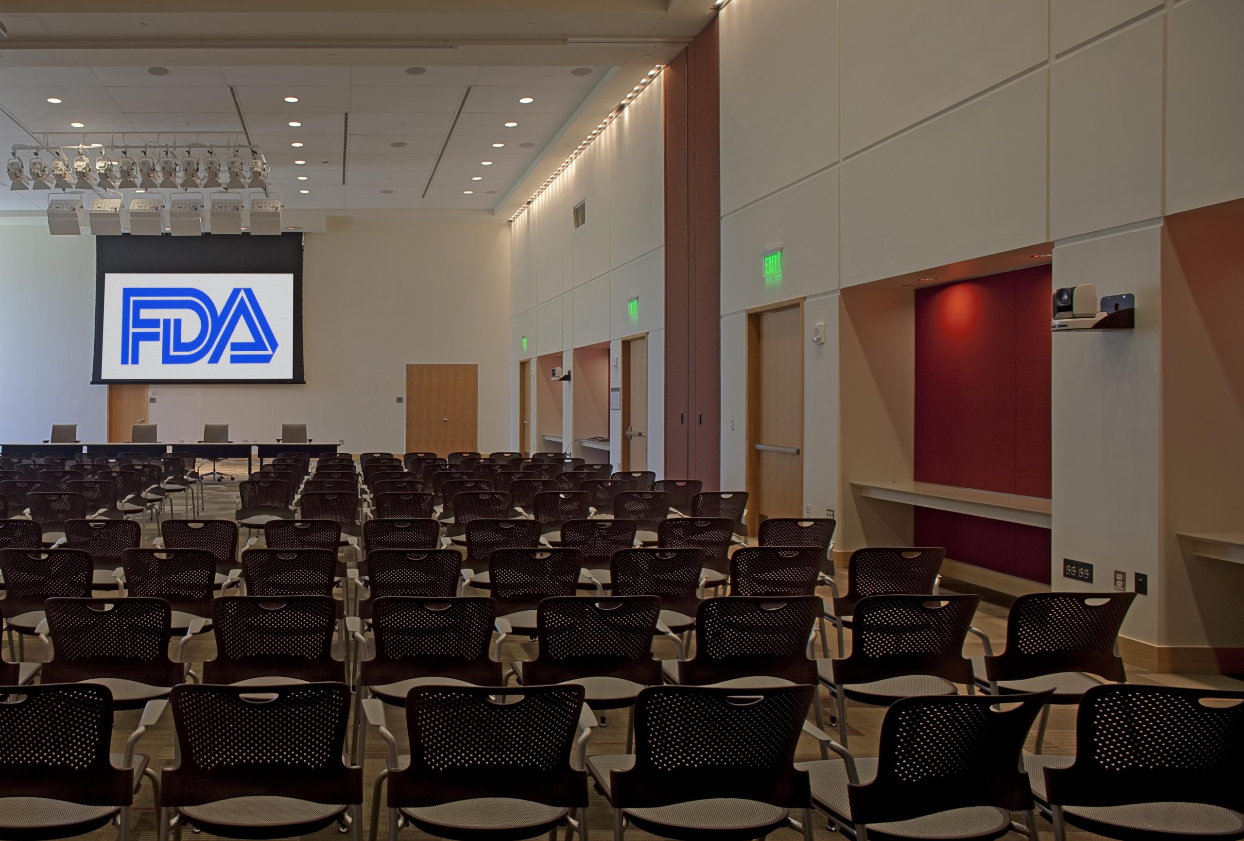 Rows of empty chairs face a projection screen showing the FDA logo in a large conference room.