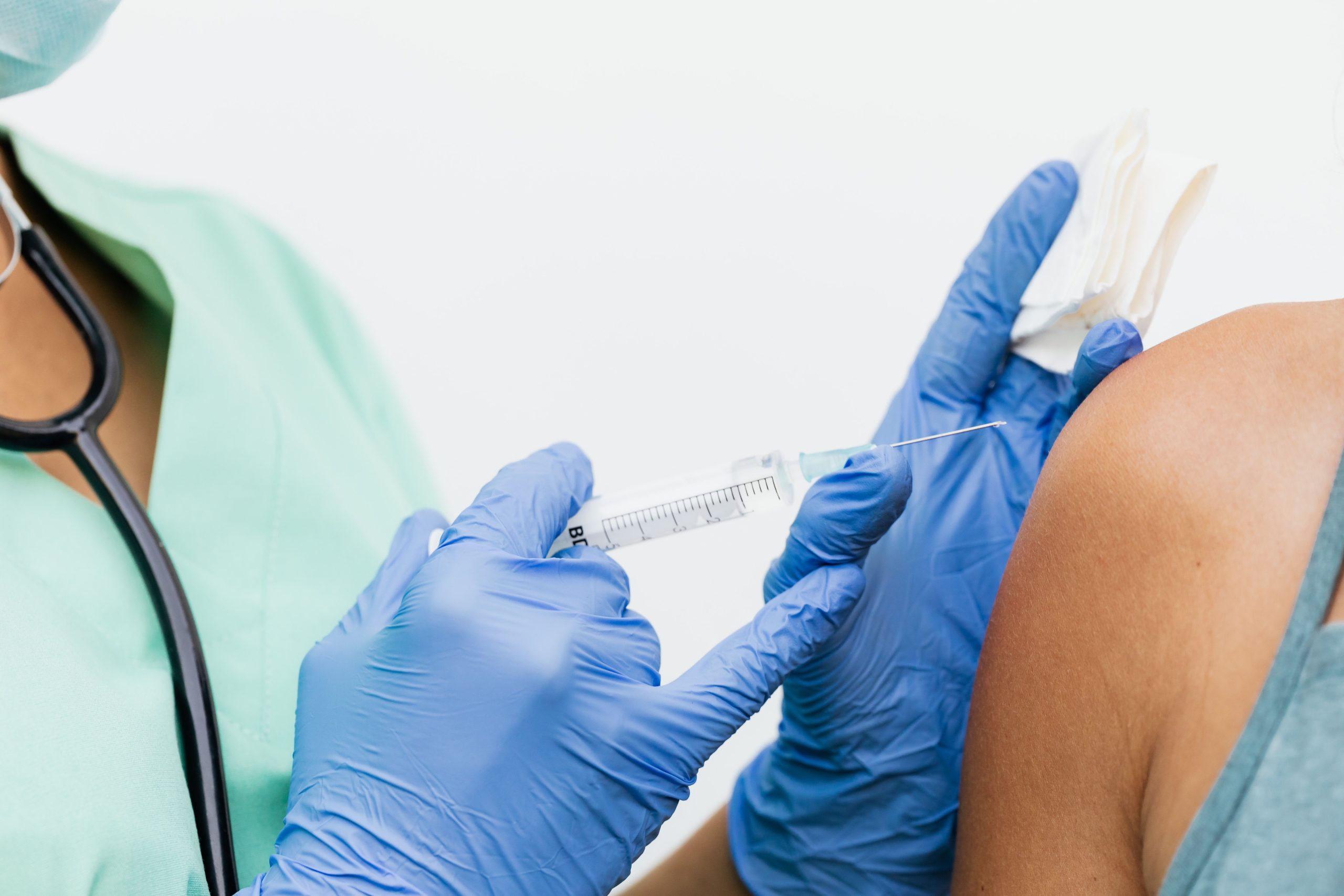 A healthcare worker in gloves administers a vaccine injection into a patient's upper arm.