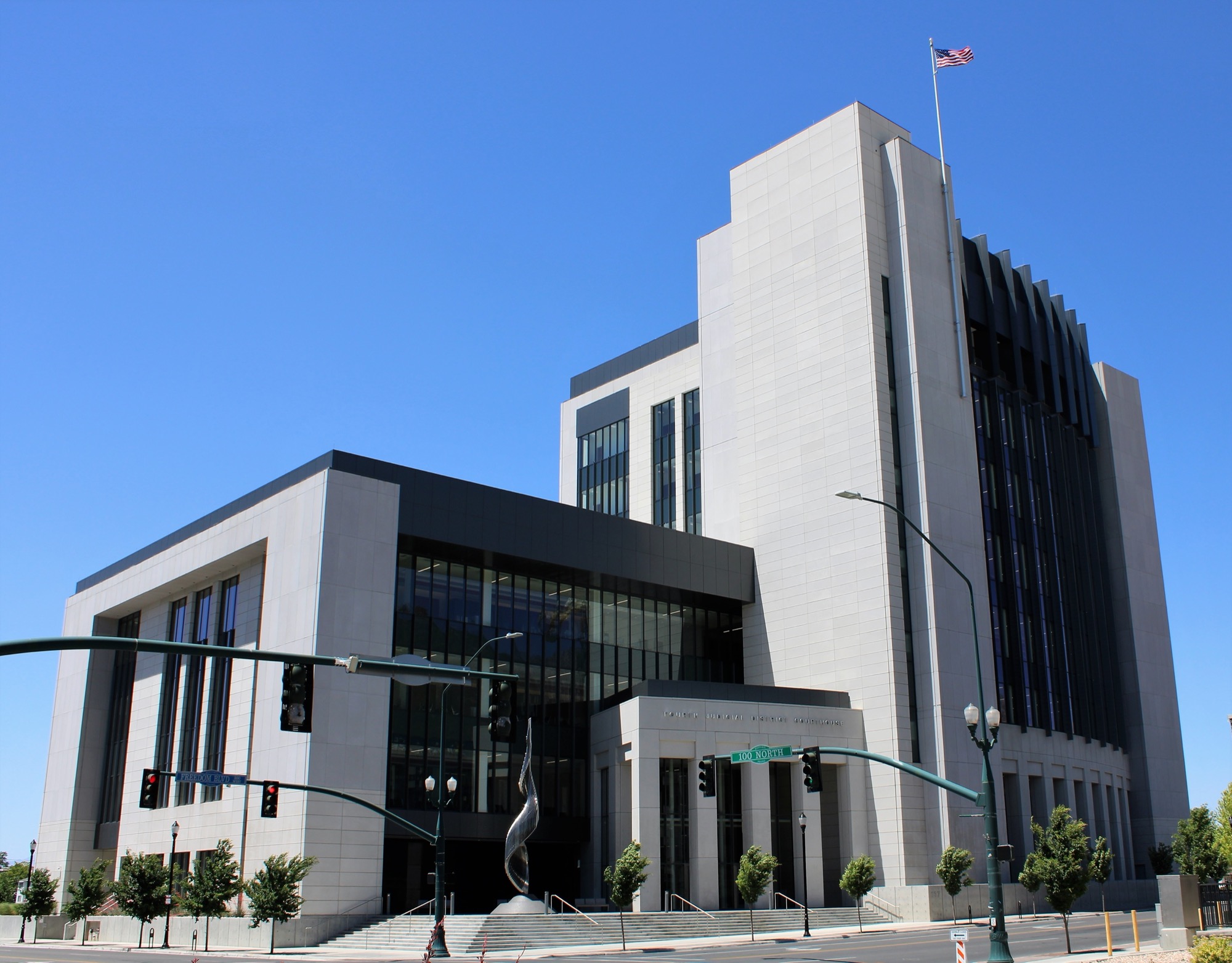 The modern stone-and-glass Fourth Judicial District Courthouse in downtown Provo, Utah, under a clear blue sky, with an American flag on its roof.