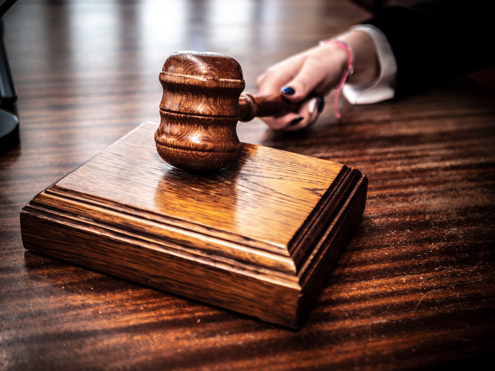 A wooden gavel resting on its sound block on a courtroom desk, held by an unidentifiable hand.