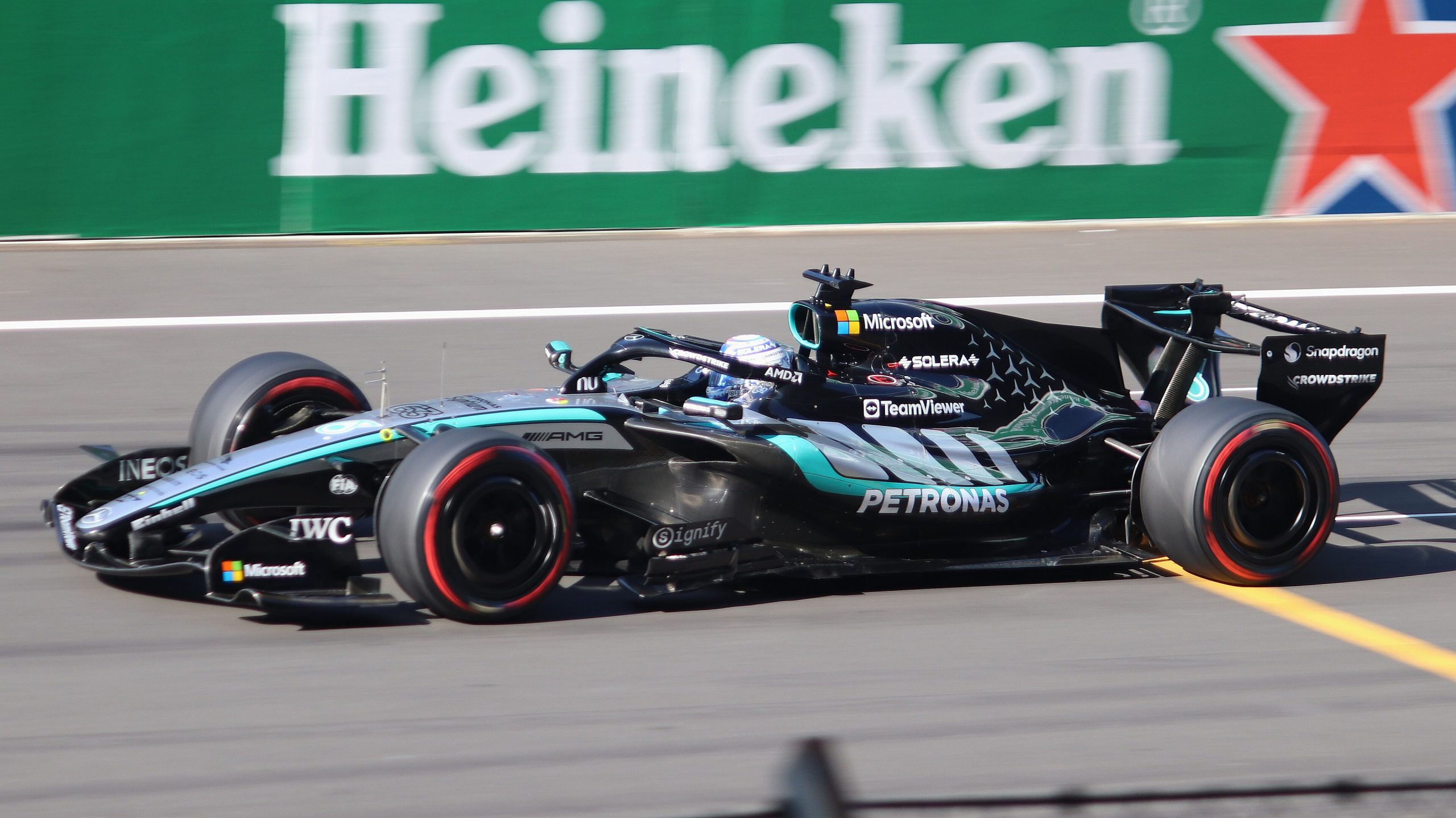 George Russell's black Mercedes Formula 1 car at speed on track during qualifying, with a trackside advertising board behind it.