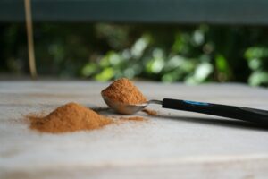 A small pile of ground cinnamon beside a measuring spoon filled with cinnamon on a wooden board.