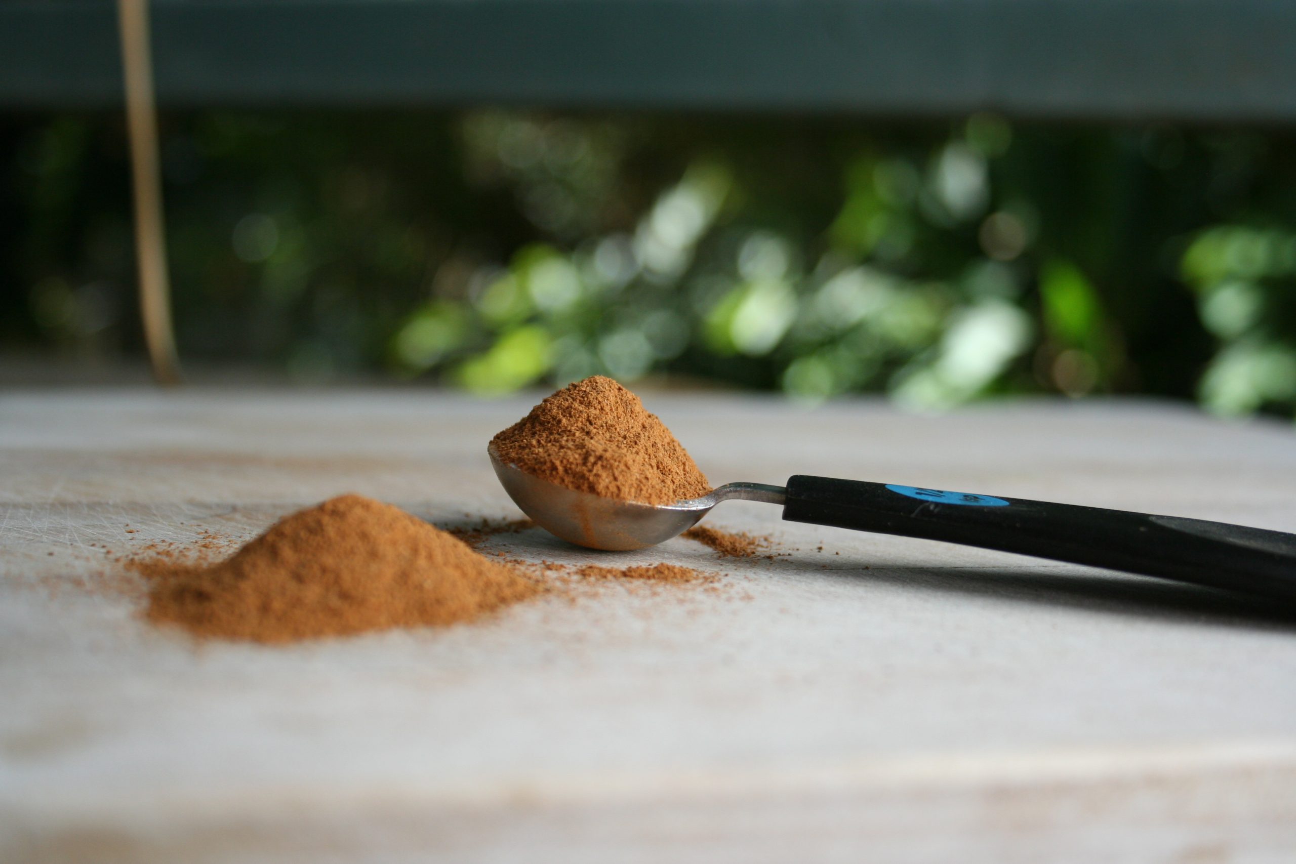 A small pile of ground cinnamon beside a measuring spoon filled with cinnamon on a wooden board.