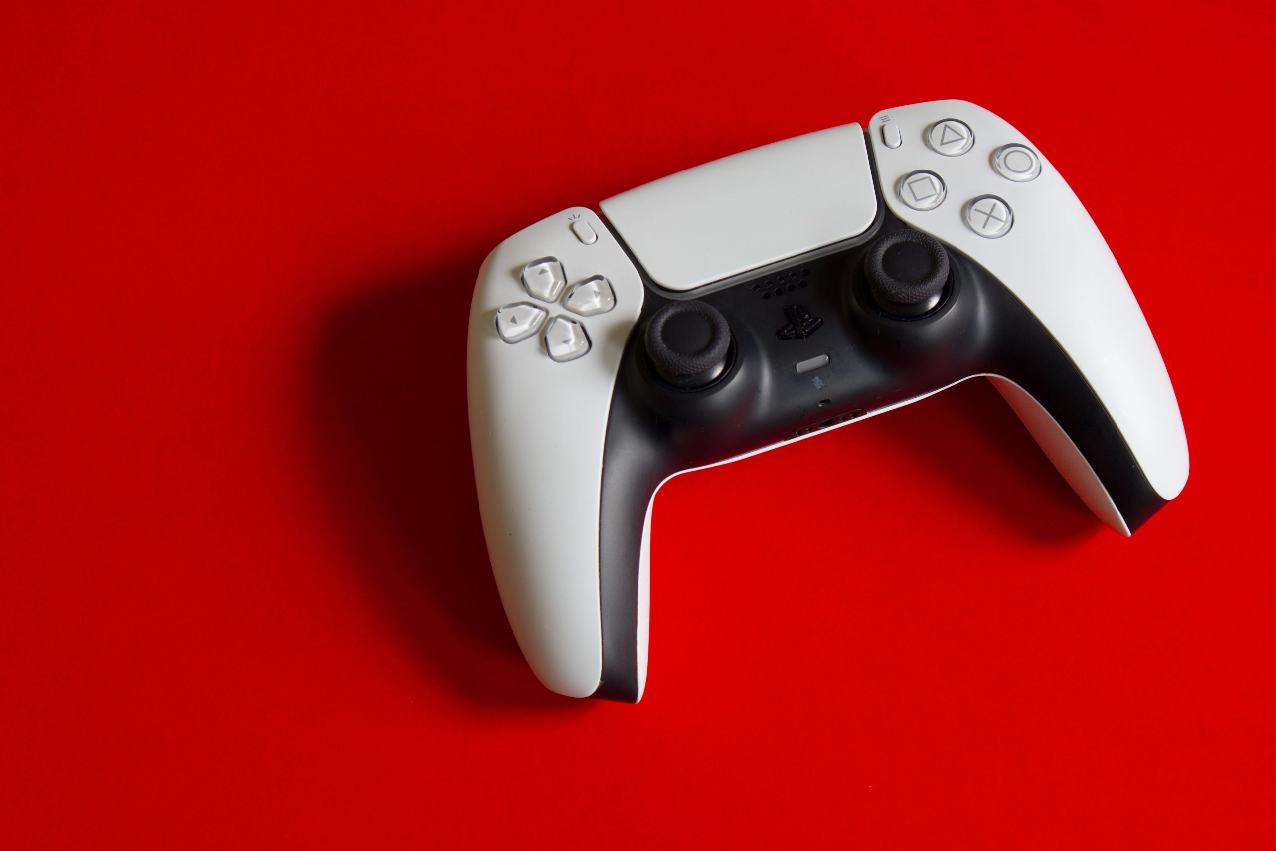 A white PlayStation 5 DualSense wireless controller on a red background