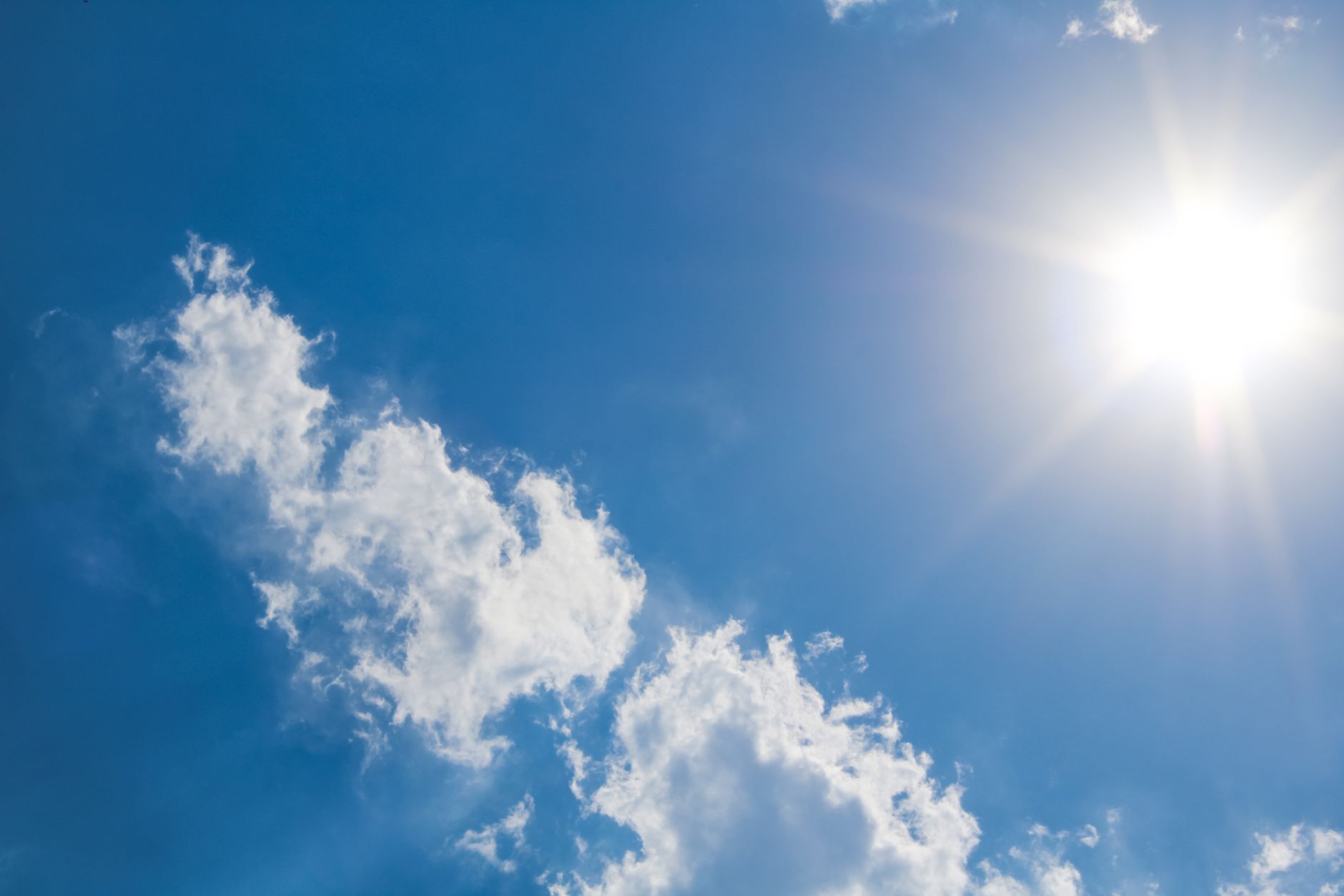 The sun glaring through a clear blue sky above scattered white clouds