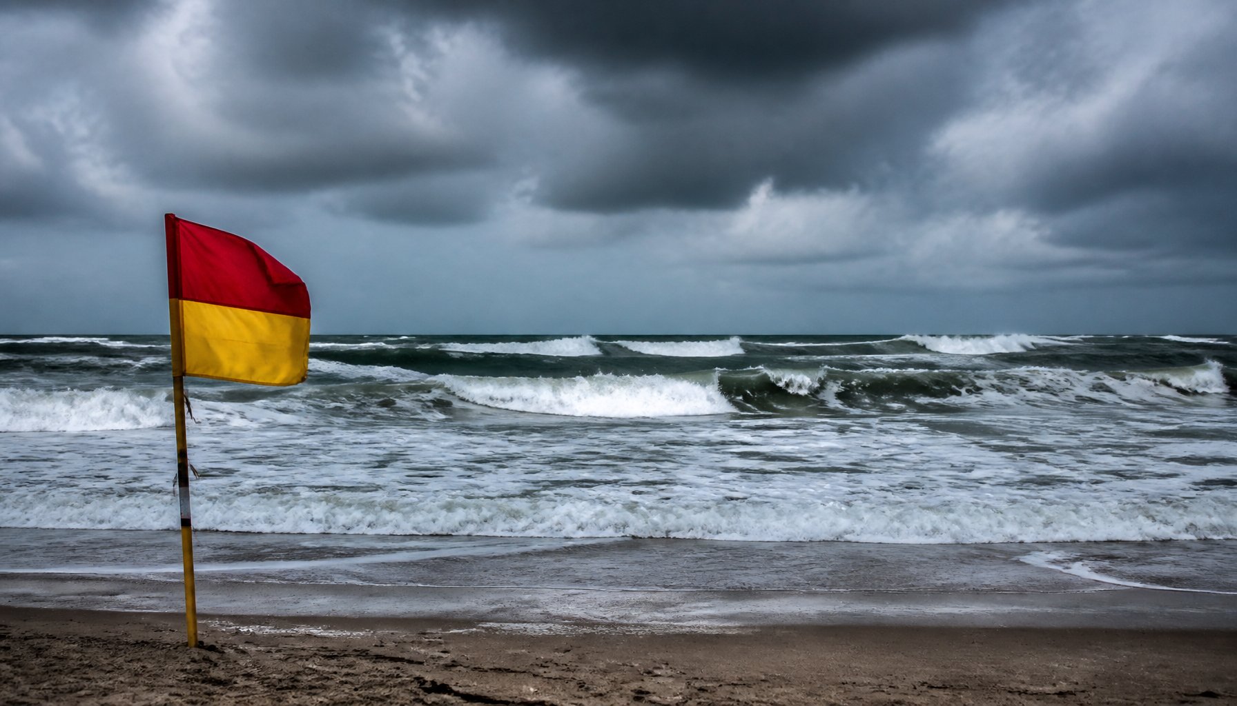 AI-generated illustration: rough surf and a beach warning flag under a stormy sky