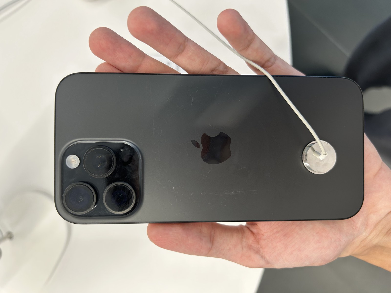 The back of a black iPhone 16 Pro Max held in a hand, showing its triple-camera array