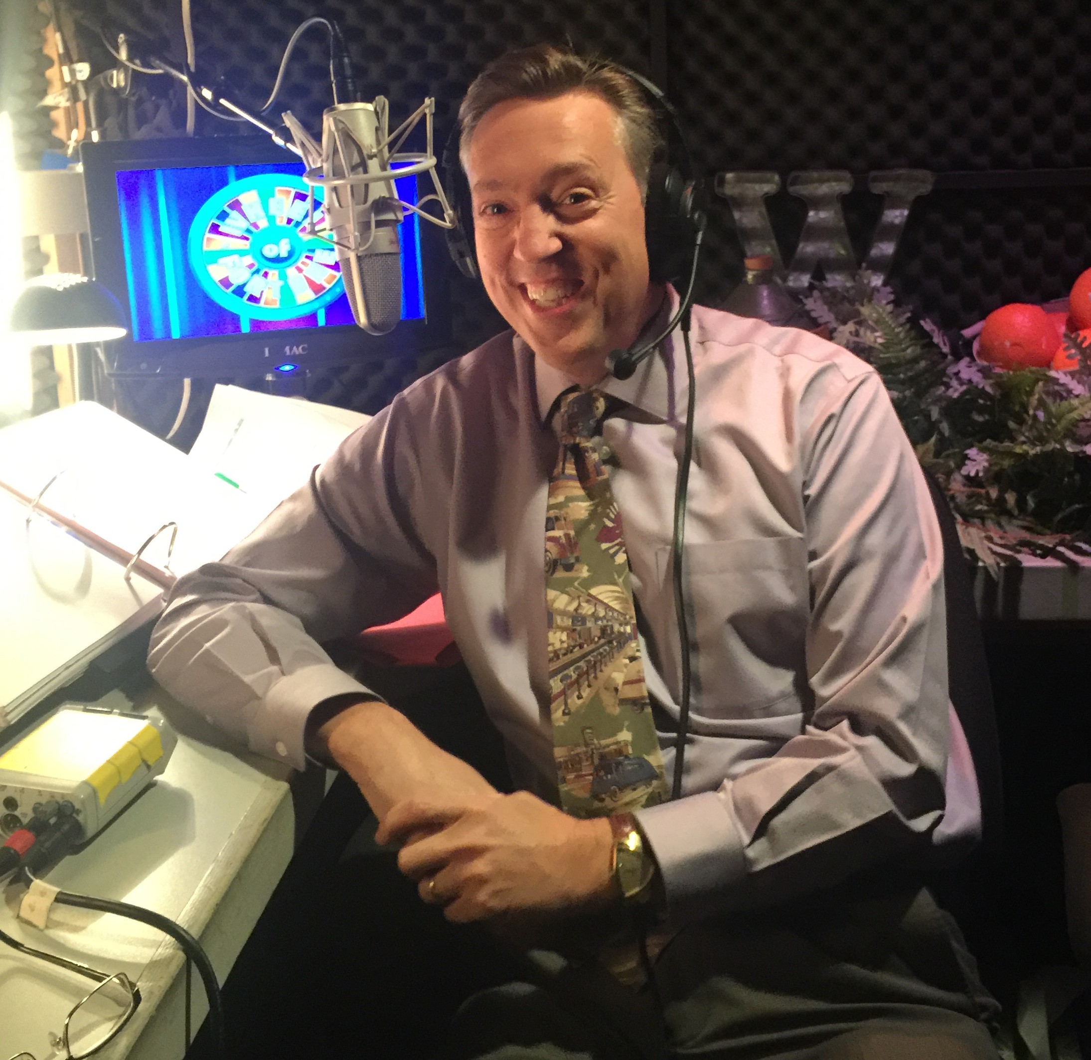 Jim Thornton, announcer on Wheel of Fortune, smiling at the microphone in the announcer's booth shortly before a taping