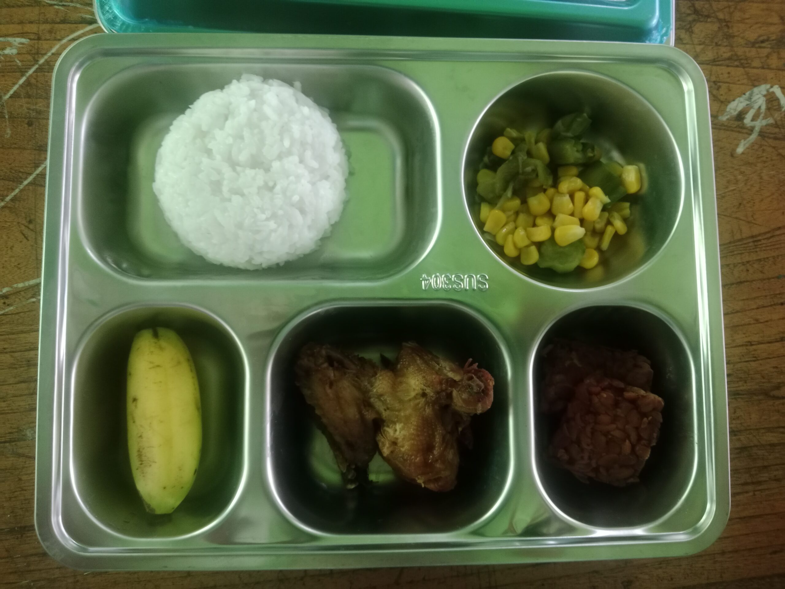 A stainless-steel tray of rice, chicken, tempeh, vegetables and a banana served under Indonesia's free school meal program