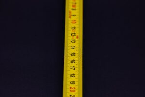 A yellow measuring tape with black and red numbers laid across a dark blue background.
