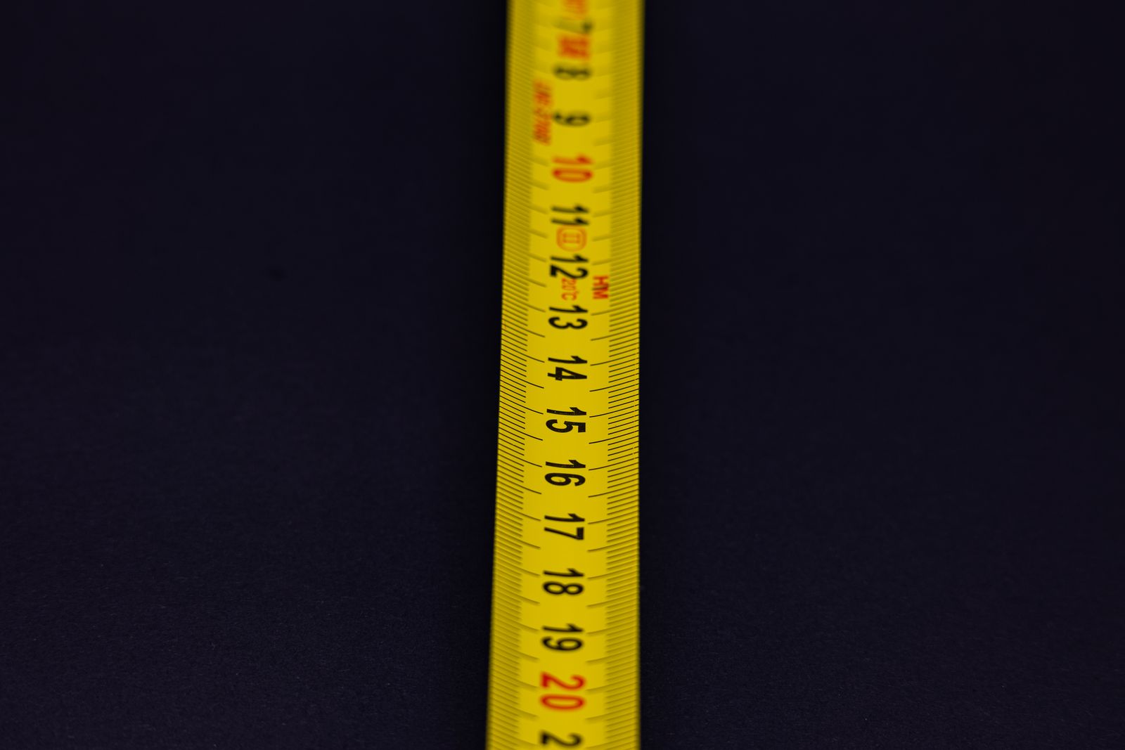 A yellow measuring tape with black and red numbers laid across a dark blue background.