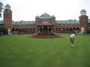 The domed brick clubhouse of Medinah Country Club behind a putting green, with a golfer putting in the foreground.