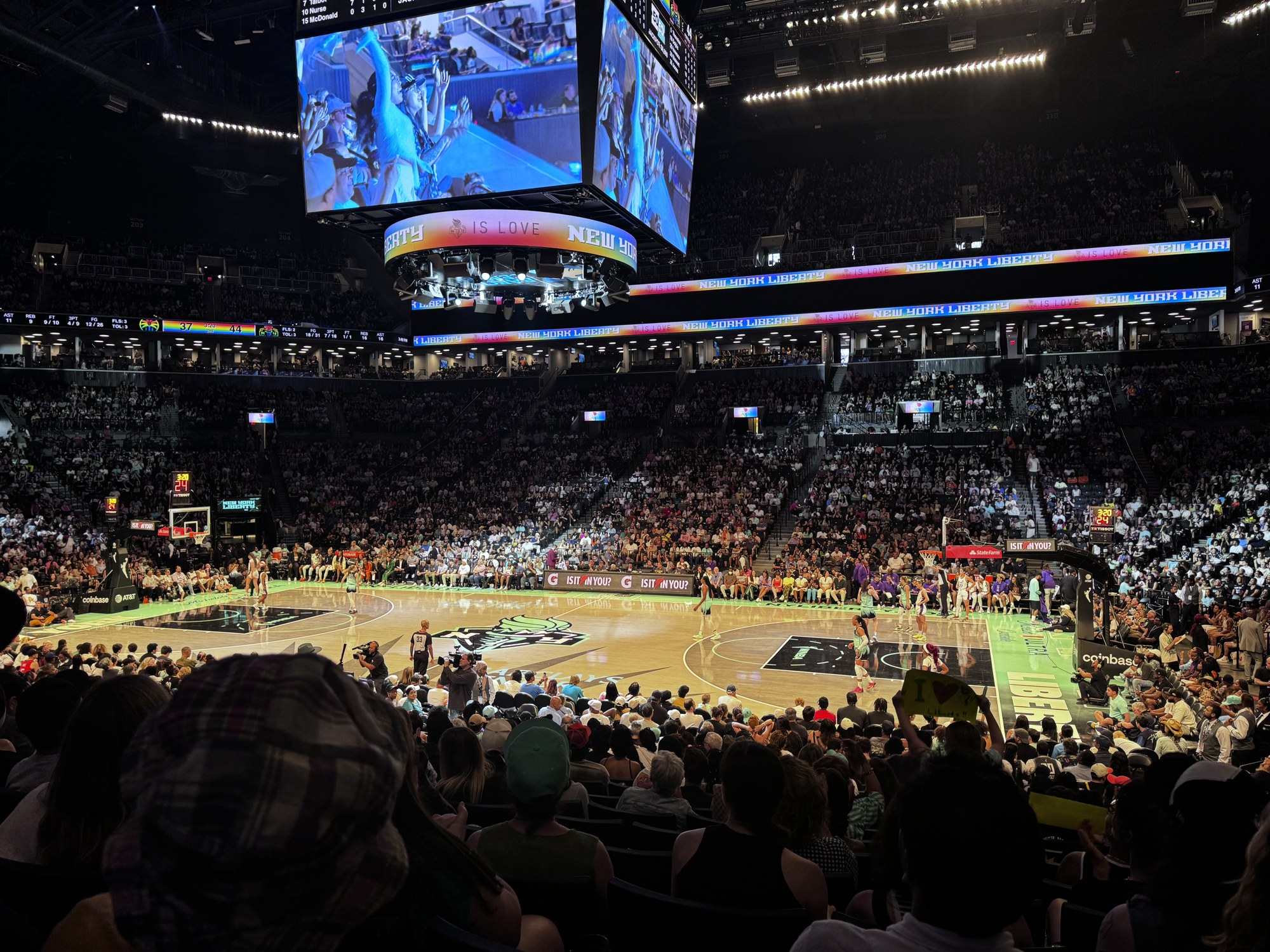 A packed Barclays Center in Brooklyn during a New York Liberty home game, with the court, the center-hung video board and New York Liberty signage on the ribbon boards.