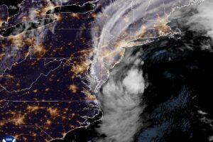 Night satellite image of the U.S. East Coast with city lights, showing the nor'easter's cloud mass swirling off Virginia and the Delmarva Peninsula and cloud bands streaming north over New Jersey, New York and New England.