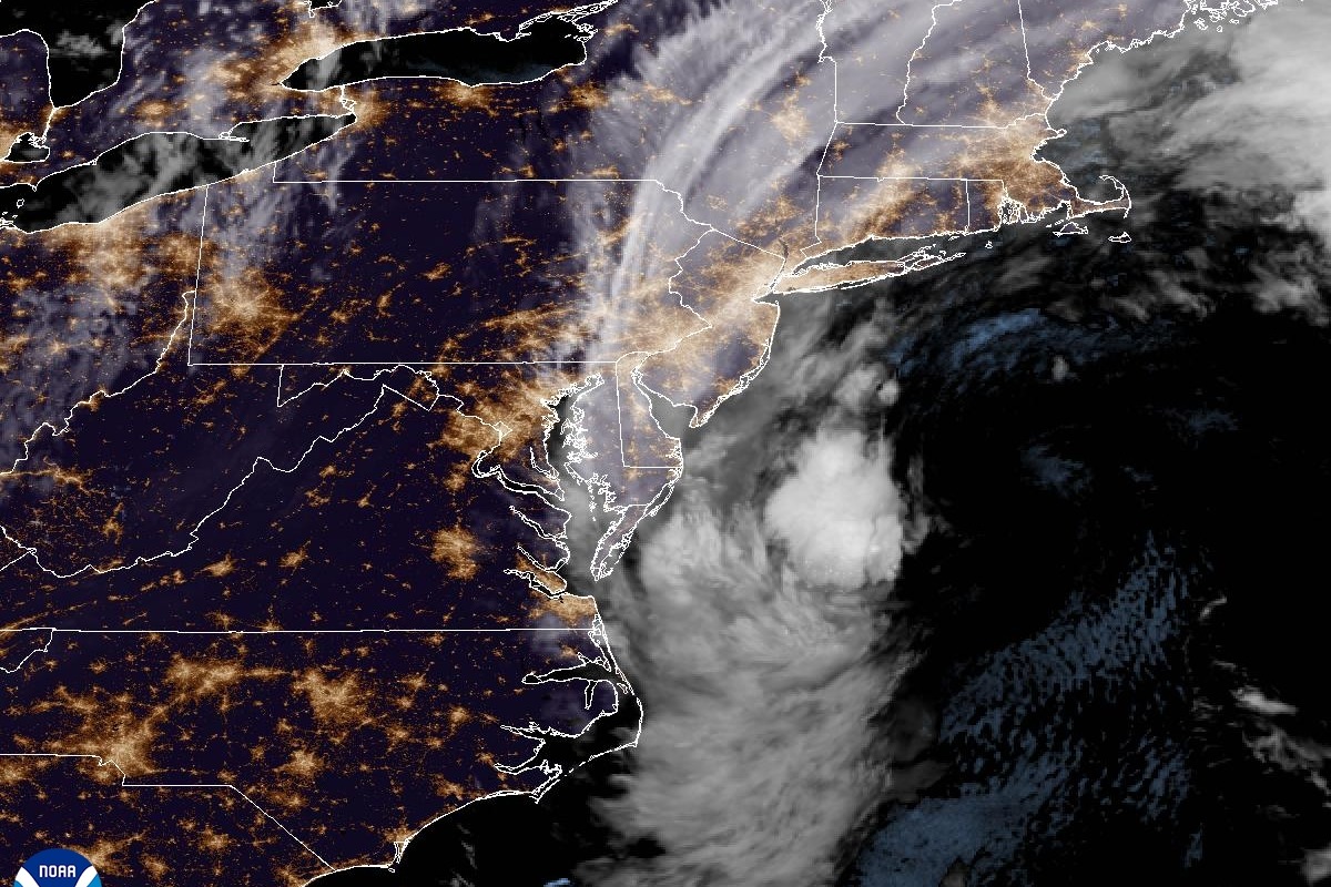 Night satellite image of the U.S. East Coast with city lights, showing the nor'easter's cloud mass swirling off Virginia and the Delmarva Peninsula and cloud bands streaming north over New Jersey, New York and New England.