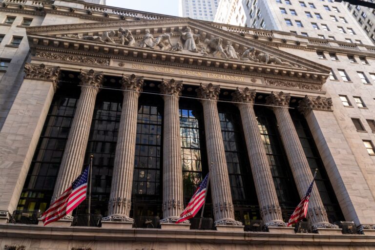 The New York Stock Exchange building facade in New York City, with American flags flying at its columned entrance.