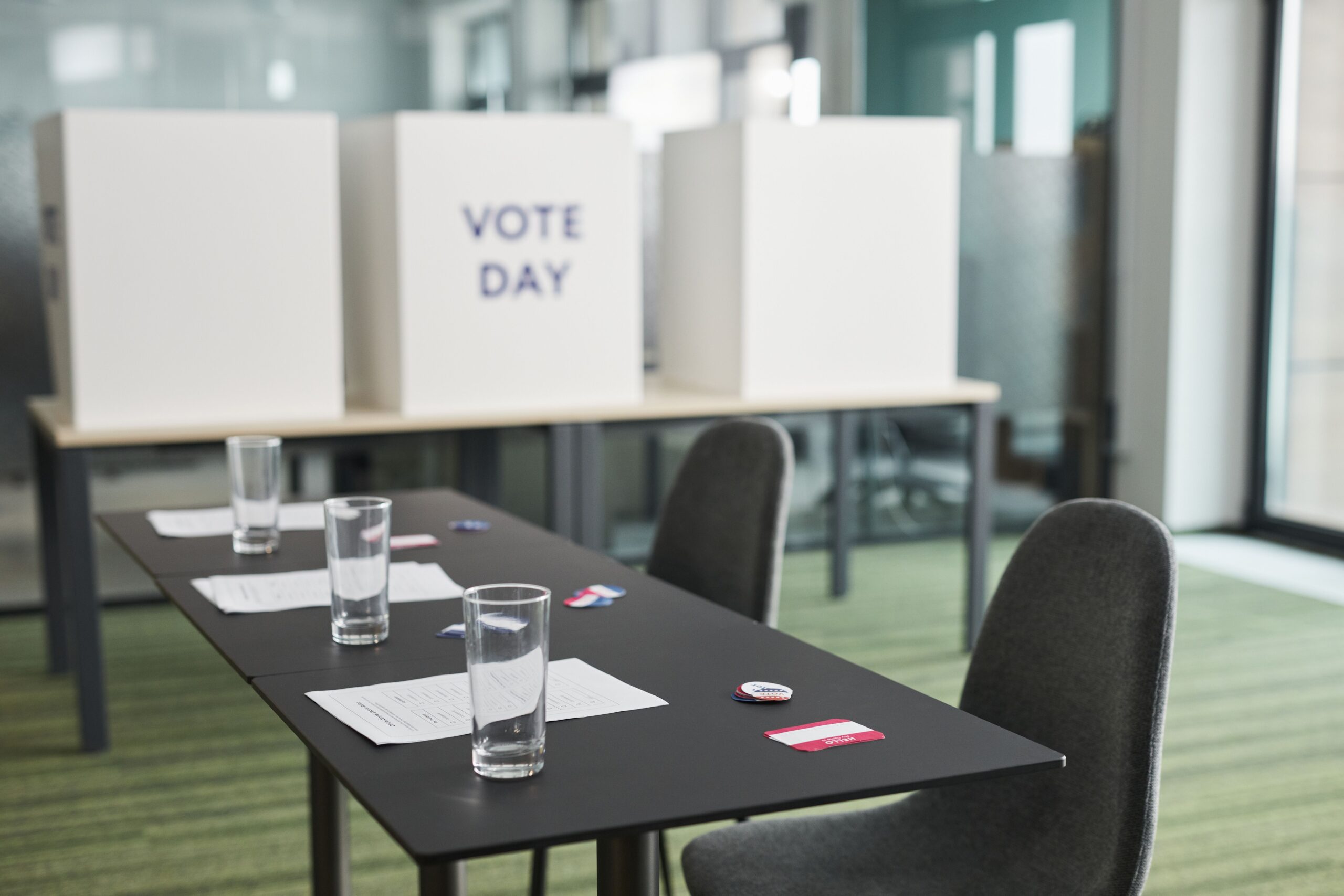 A prepared polling place: voting booths marked Vote Day behind a table with blank ballots and I Voted stickers