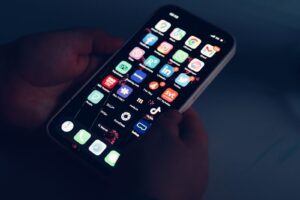 Hands holding a smartphone in a dark room, its home screen showing app icons including TikTok, Instagram and Facebook.