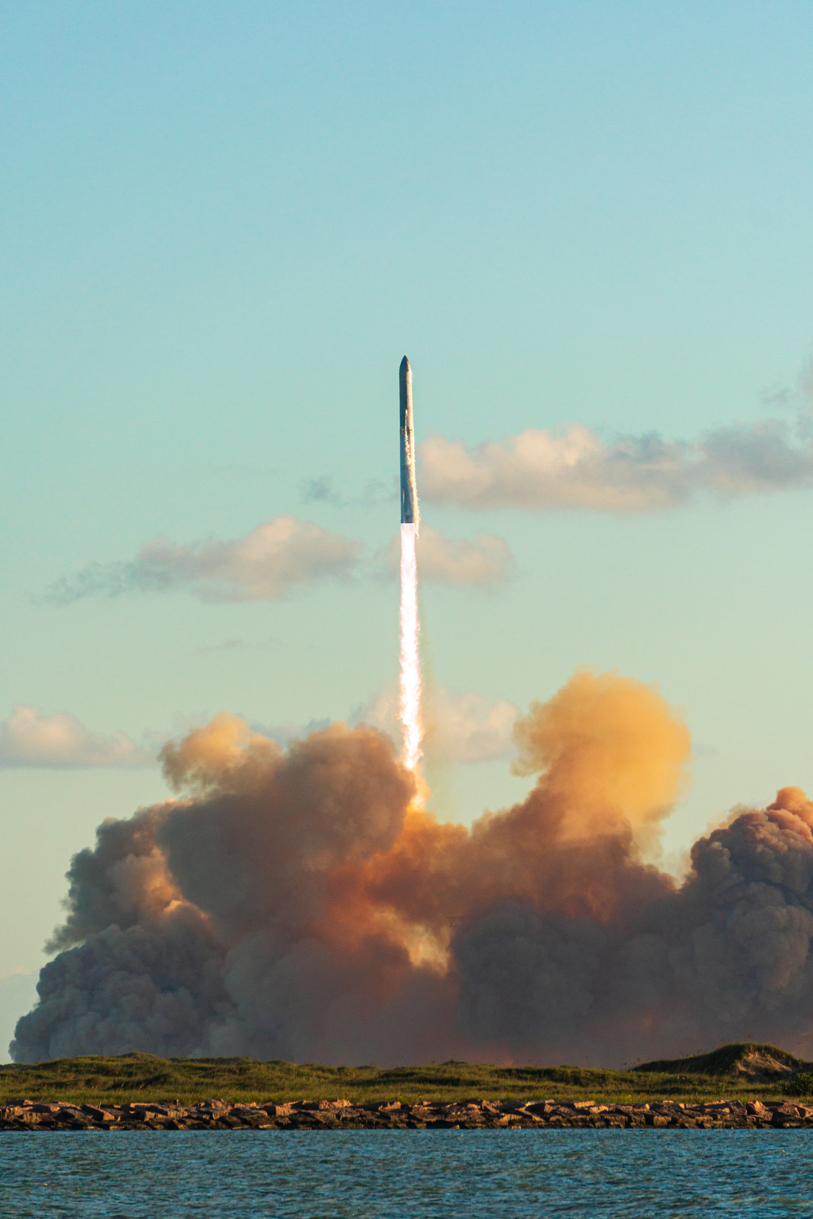 A SpaceX Starship rocket rises on a bright exhaust plume above a large cloud of smoke at Starbase, Texas, during its 11th flight test.