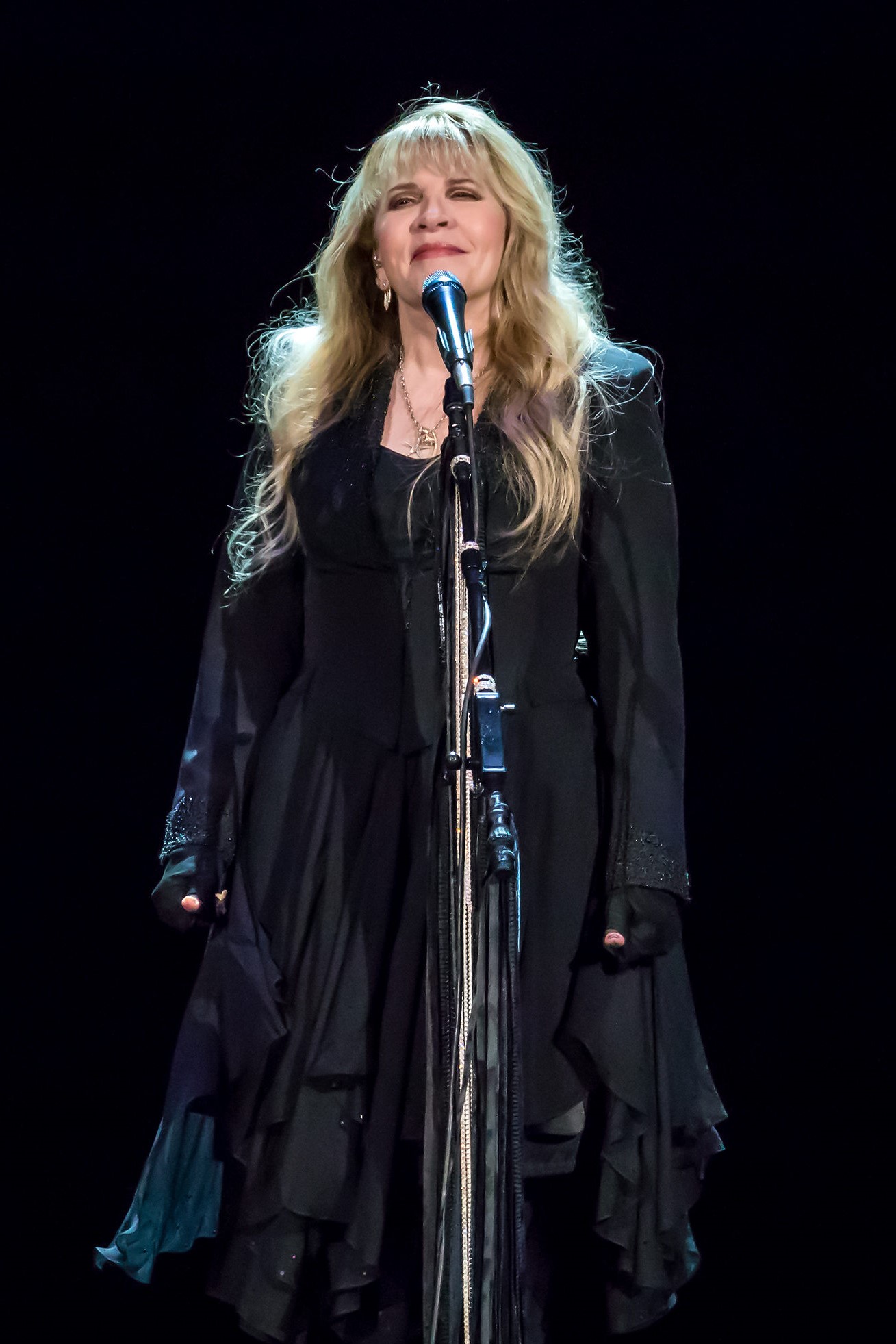 Stevie Nicks performing on stage in a black outfit, singing into a microphone