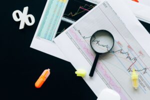 Photo: High-angle view of financial charts, showcasing stock market analysis with magnifying glass and highlighters.