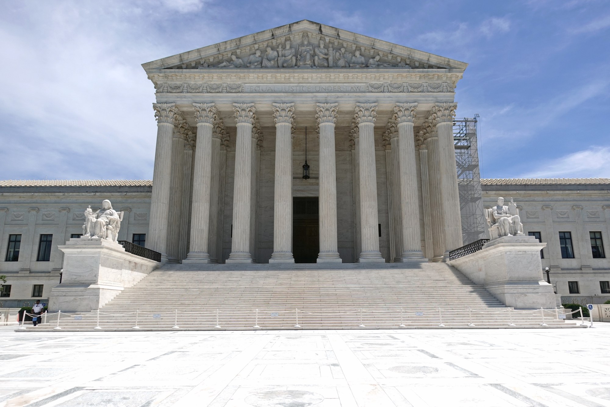 The white marble west facade of the U.S. Supreme Court Building in Washington, with its columns, steps and seated statues, under a blue sky.