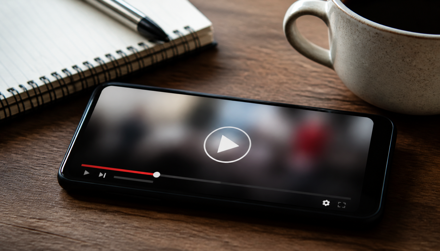 AI-generated illustration: a smartphone showing a paused, blurred video on a desk next to a notebook and coffee, symbolizing a viral online video.